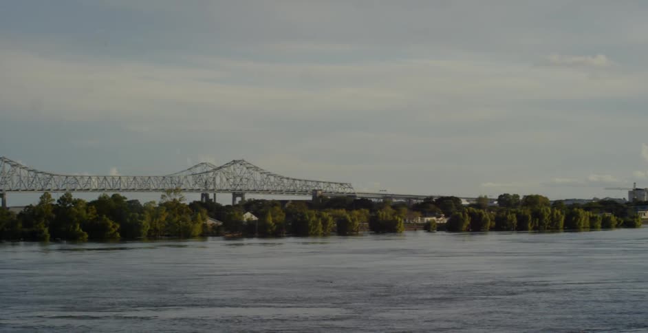A lengthy bridge crosses a large river to connect to a metropolitan area with numerous skyscrapers