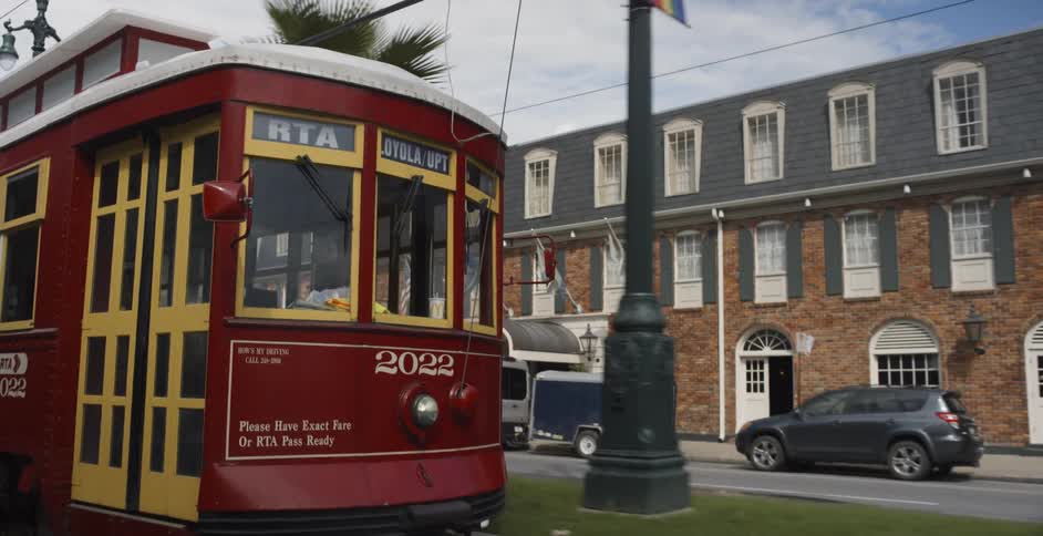 A red trolley going down a street with palm trees in the median
