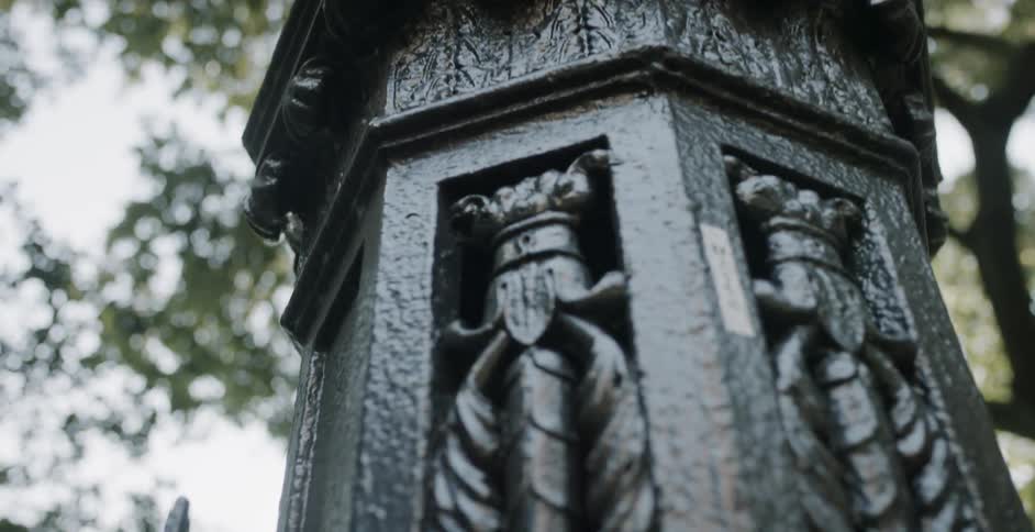 Wrought iron lamp post and gate sit near a tall tree