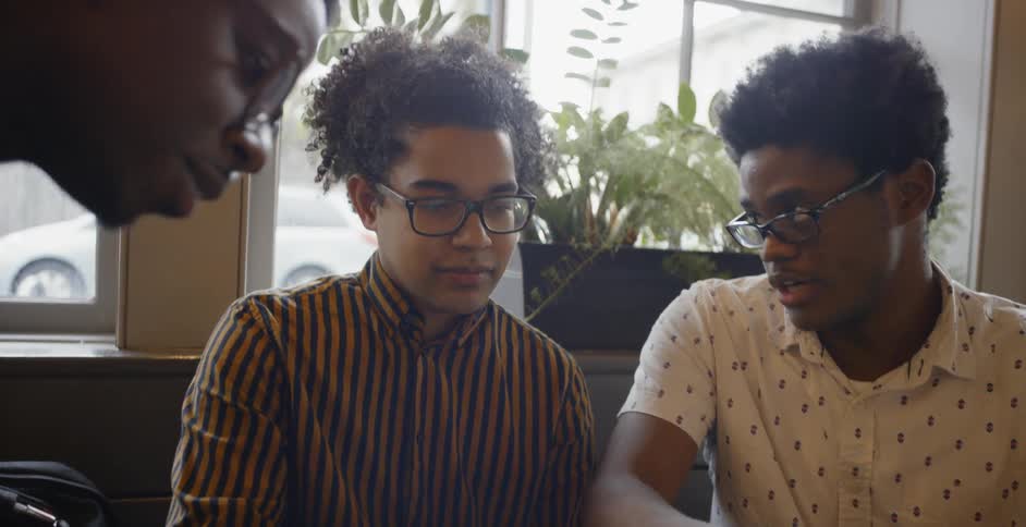 Three young black men talk over a laptop