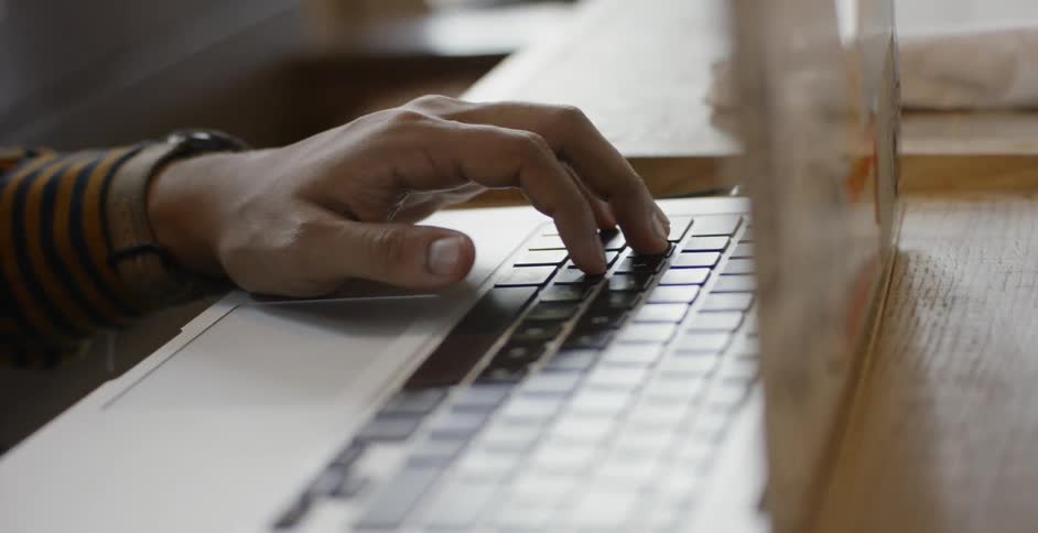 A person sitting at a table with a laptop and a drink