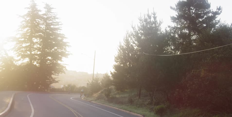 A person on a bike rides in the bike lane on a winding tree lined two lane road