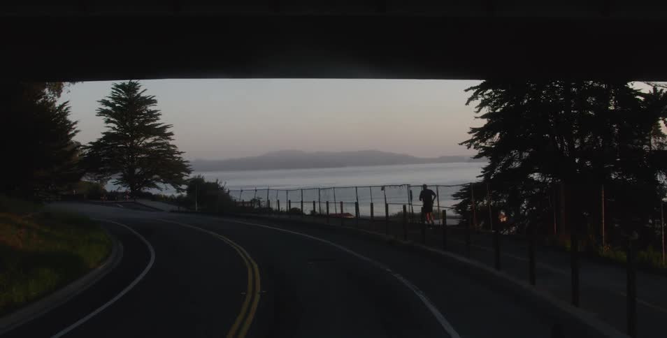 A man jogging along a path next to a road and a river
