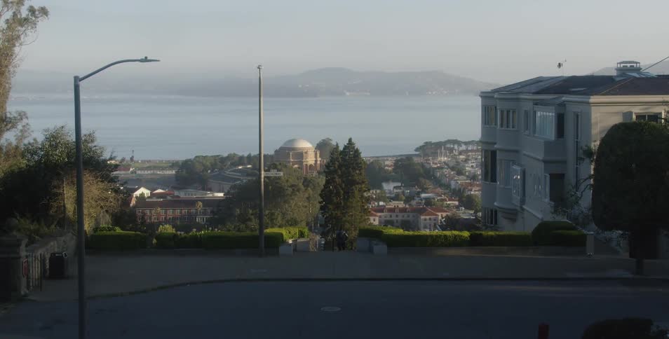 A city street with a pathway down towards large houses and open water