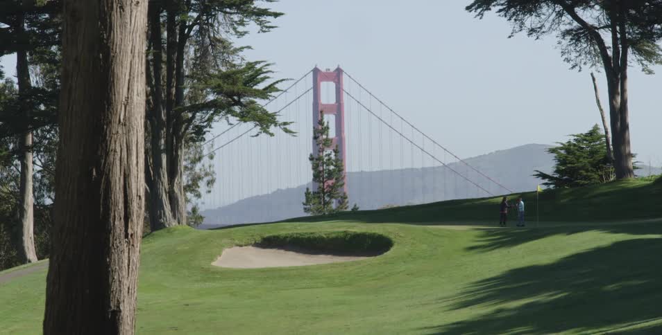 Man and woman play golf at golf course with golden gate bridge scenery on a sunny day
