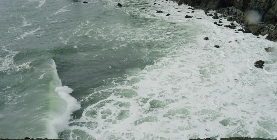 Waves break and rush to the rocky shore that's covered in sea foam