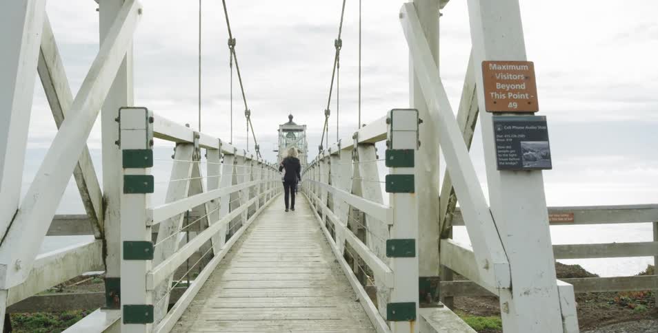 A woman walks along a white foot bridge