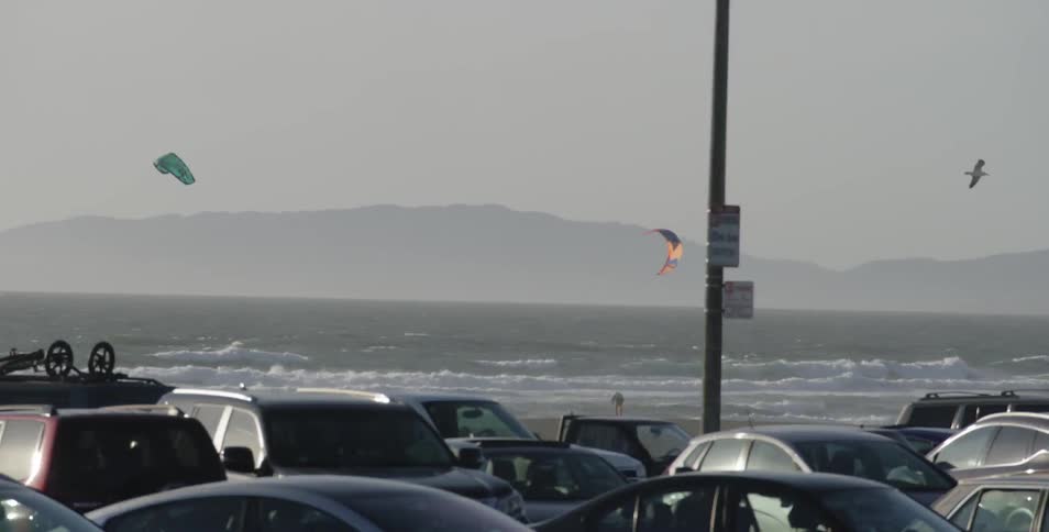 People windsurfing in the ocean near a crowded beach