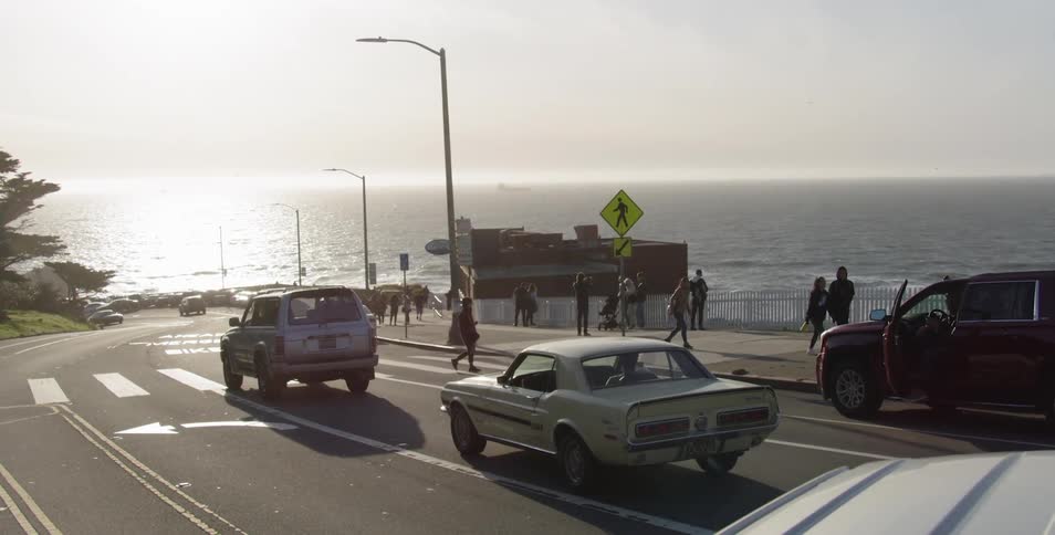 Cars drive alongside ocean at sunrise