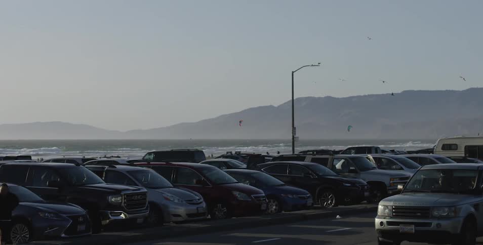 Densely packed parked cars can be seen by the road near the ocean