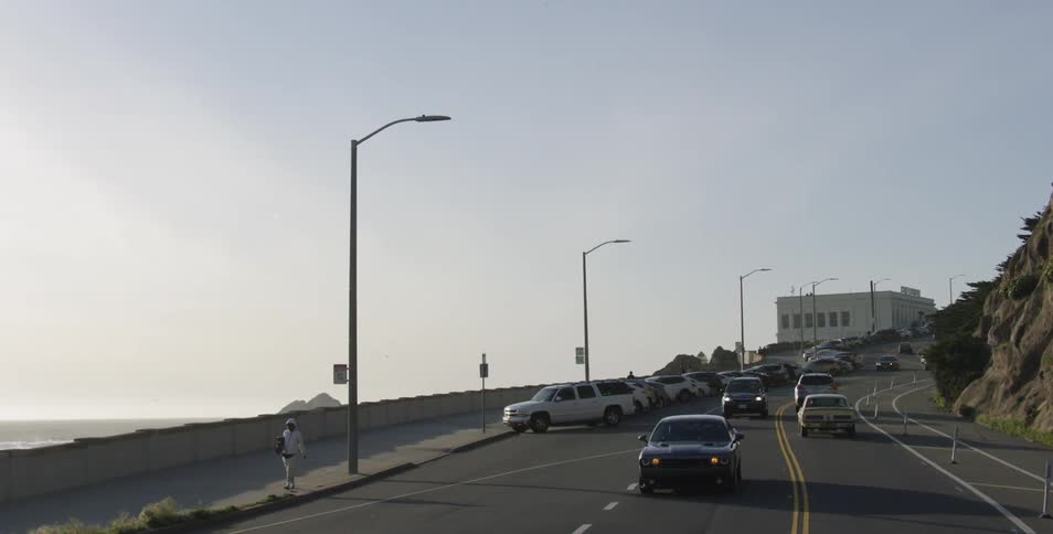 Cars drive through mountain highway next to the coast while the sun goes down