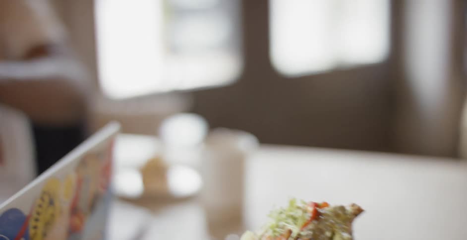 Man eats a sandwich as two other men sit across from him with a laptop