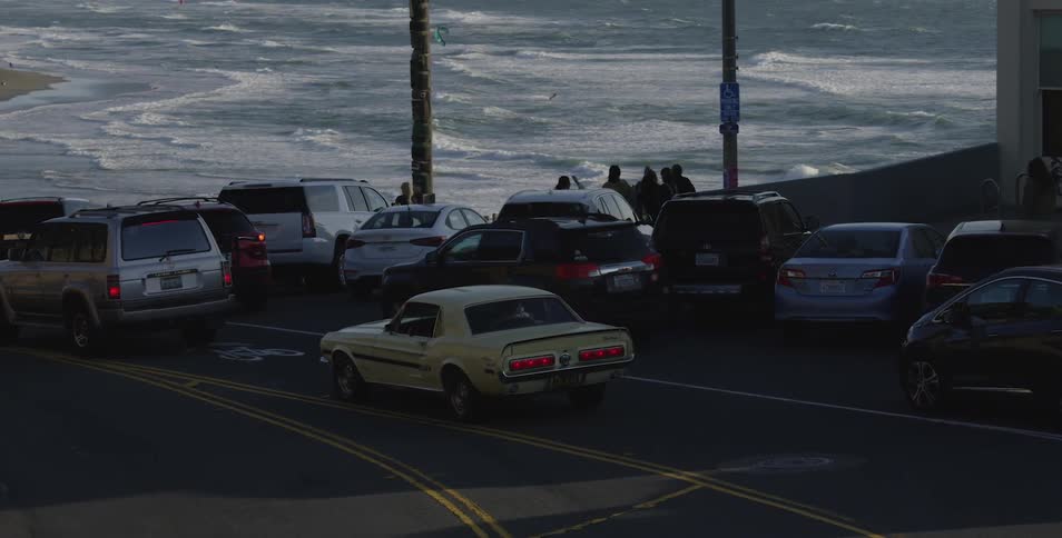 Cars drive down to the coast while the waves hitting the shore at sunset
