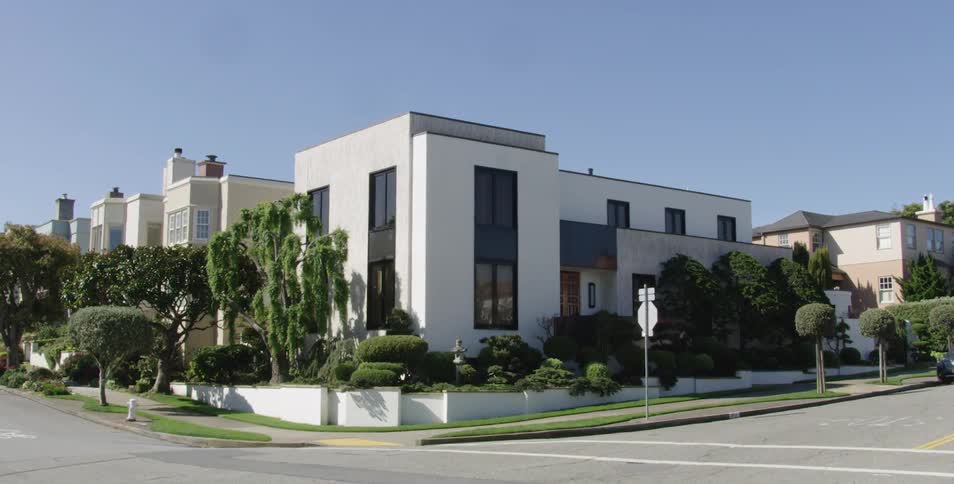 A building on a street corner with large windows and expert landscaping on a sunny day