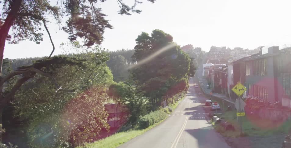 Traveling on a narrow road past homes on one side and trees and fields on the other