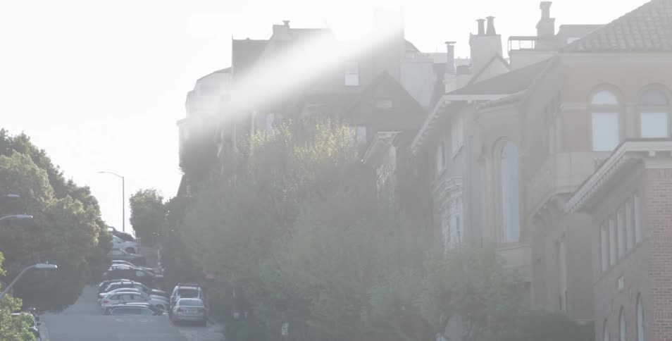 Cars parked on street in front of row of houses while sun shines