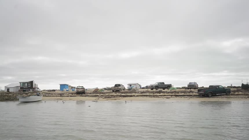 Trucks sit parked on a beach by the waterfront by a small building