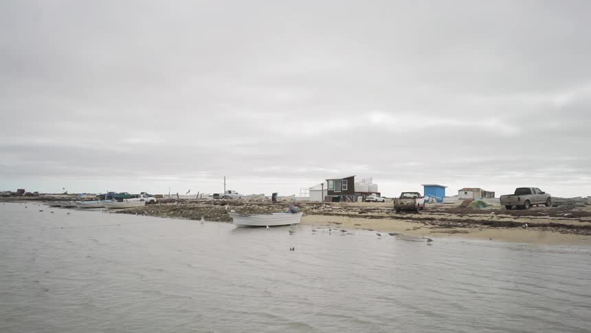 Boats sit on a beach with trucks in front of dilapidated shacks