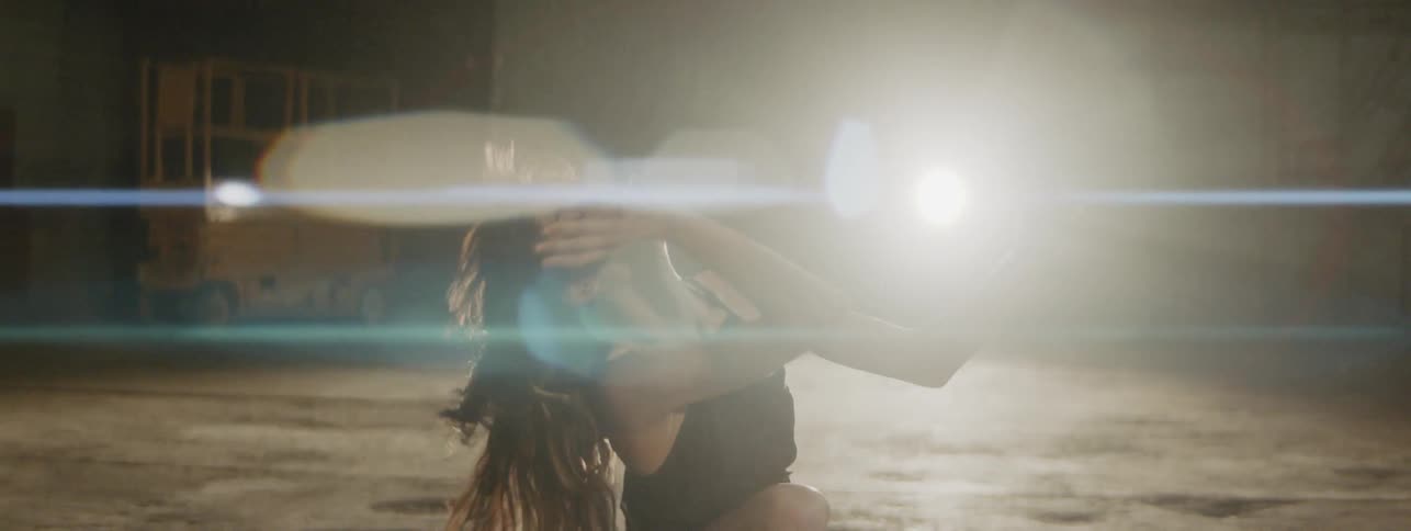 Woman dances in warehouse in front of spot light