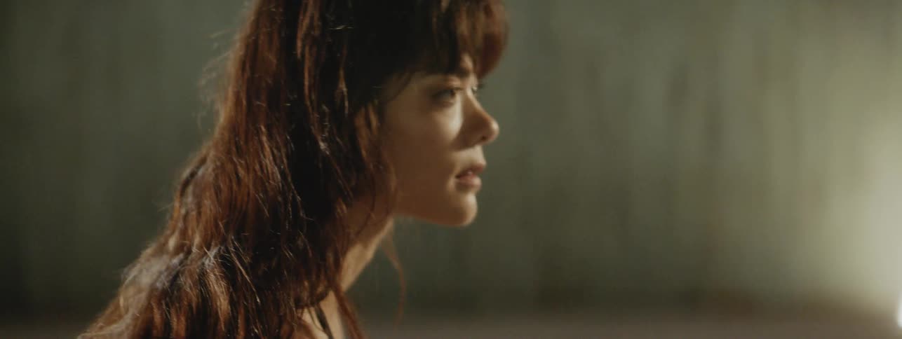 A woman with bangs and long brown hair slowly standing in a dance with bright sunlight coming through a window
