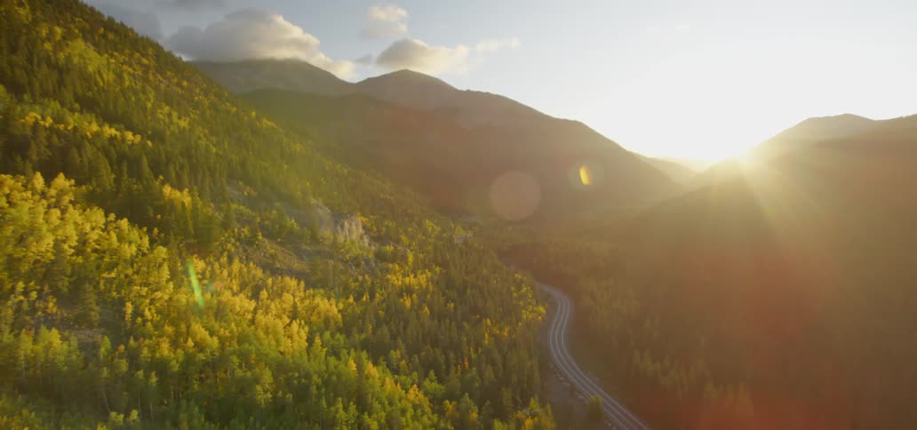 The sun shines over tree covered mountains and a winding road