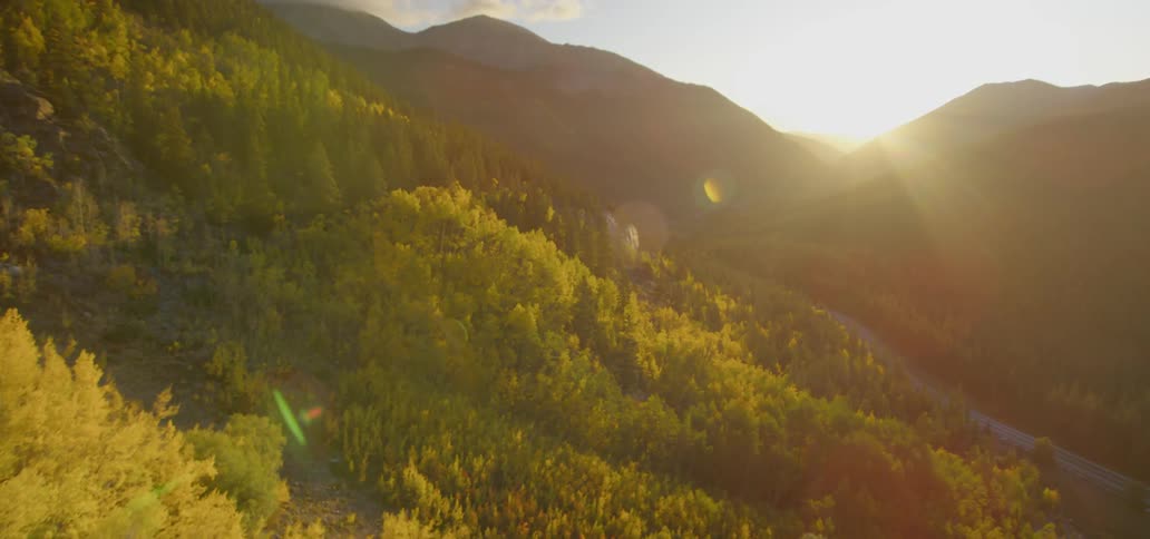Range of mountains covered with fall leaves while sun goes down behind the mountains