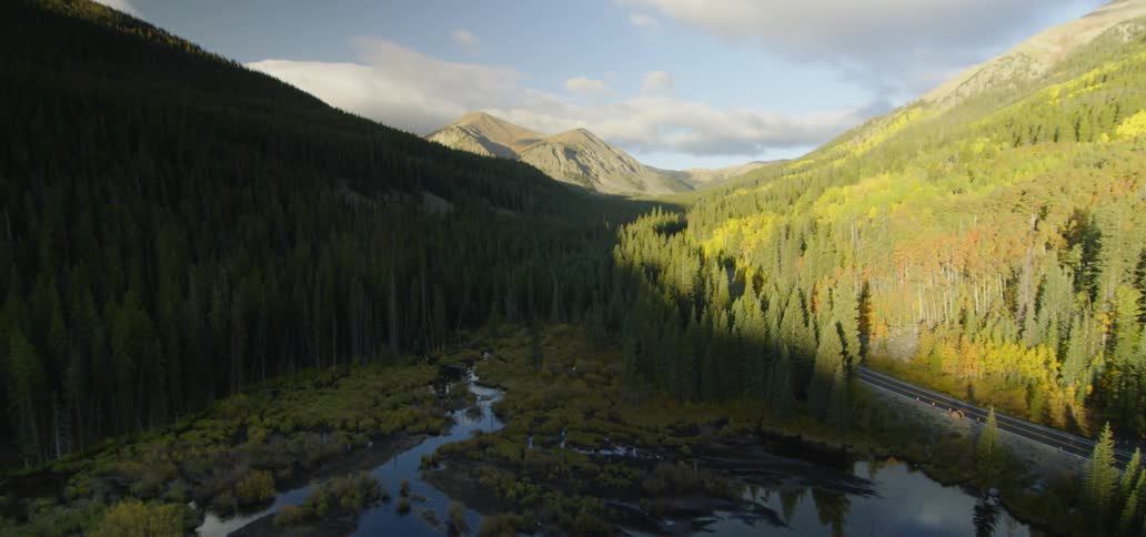 Tree lined mountains with a highway and pond