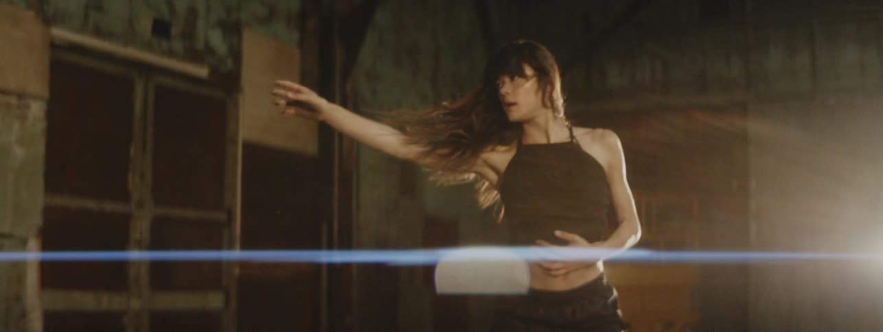 A young woman with her midriff exposed dances in front of a spotlight