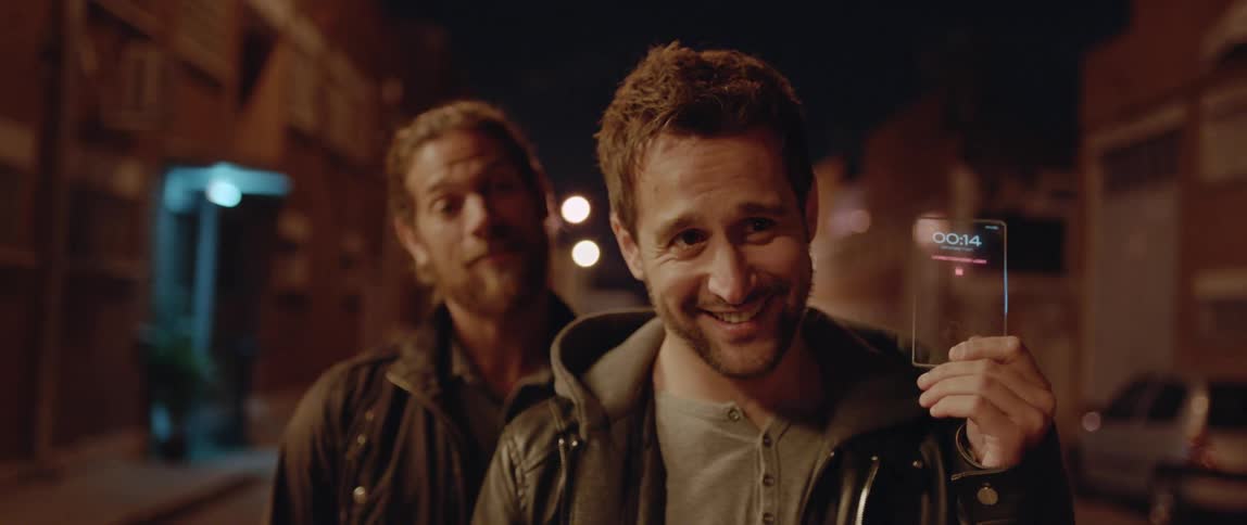 Two men stand on street at night and show device