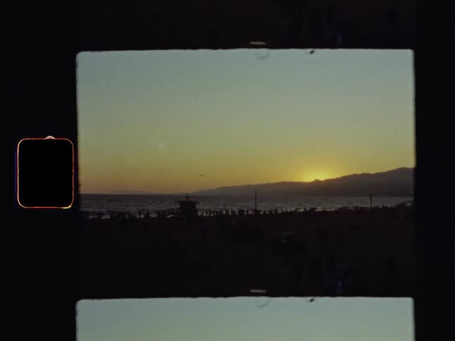 A dark view of people on a beach as the sunsets