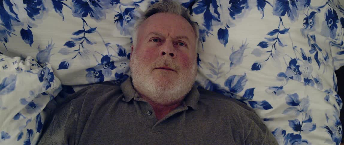 Man leaning back and laying down on bed with blue a blue floral print