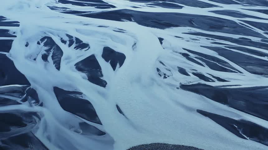 White streaks among blue black terrain with grass and mountains in the background