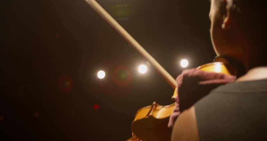 Woman who wears earrings plays on the violin under the studio lights