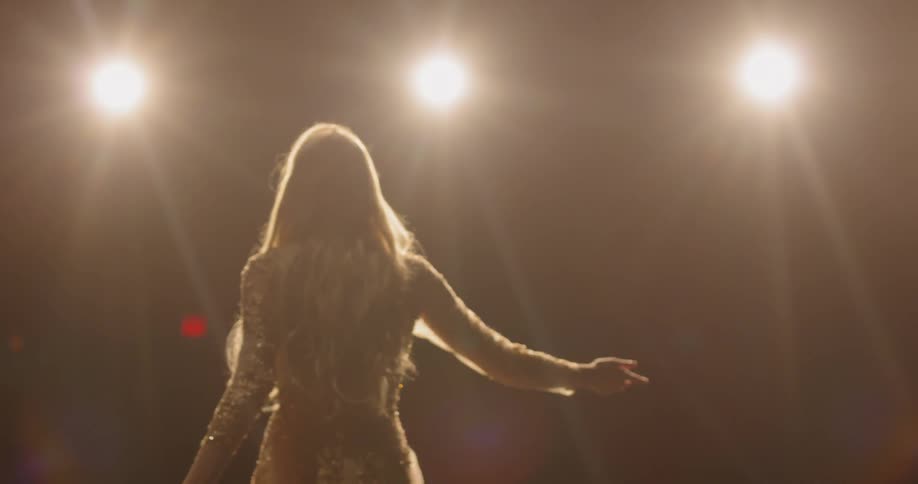 A woman wearing a gold dress performing on a bright stage