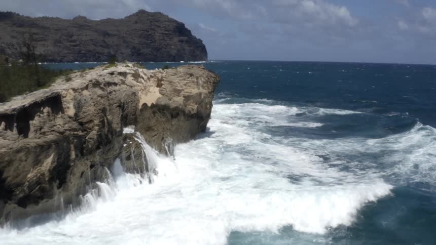 Waves of the ocean crash against big rocks and make foam on a sunny day