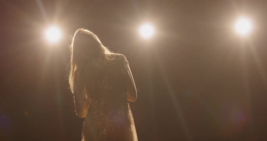 Woman in sparkly dress stands in front of bright lights