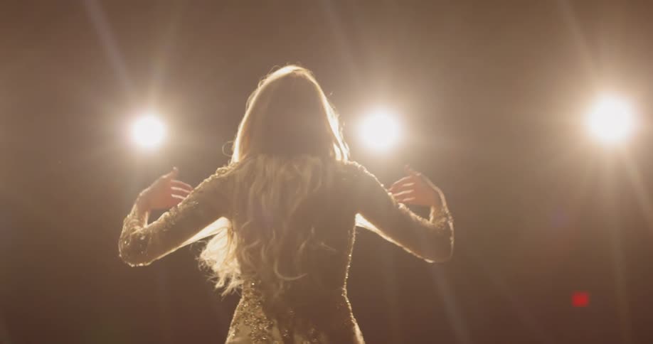 Woman sings with open arms under lights on stage