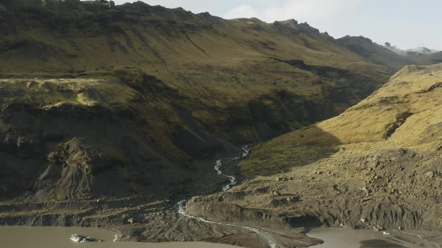 A mountain stream winds between ridges to the shore on a sunny day
