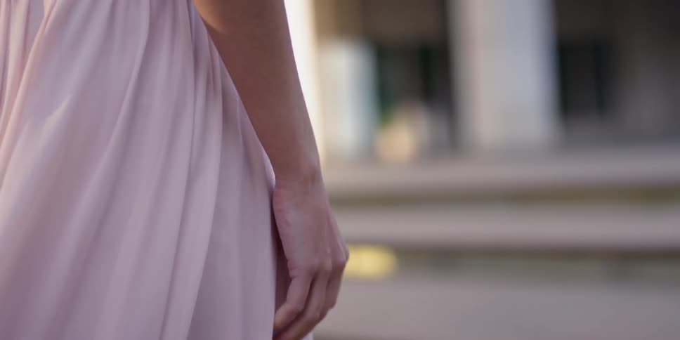 A woman wearing a pink dress walks up stairs outside at sunrise