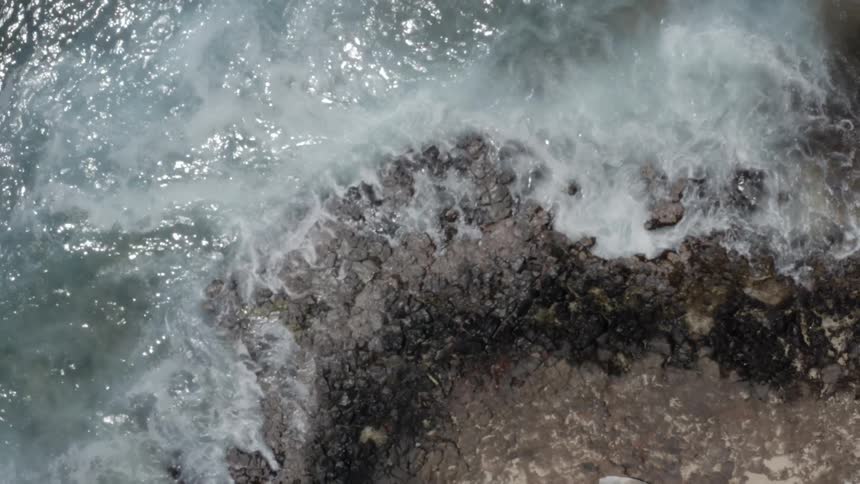 The camera zooms out of a crashing ocean beach
