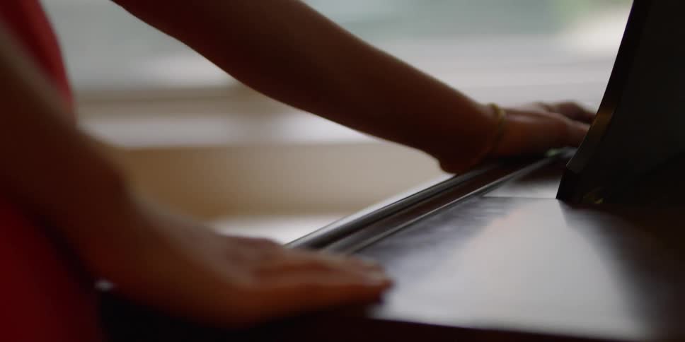 A woman running her hands along the edge of a piano