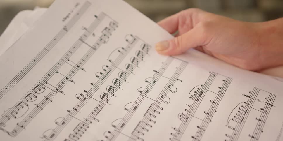 A woman sitting in a house looks at sheet music