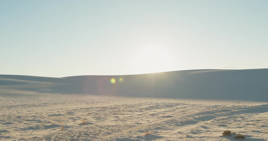 Several sand dunes line the horizon of a hot and dry desert landscape
