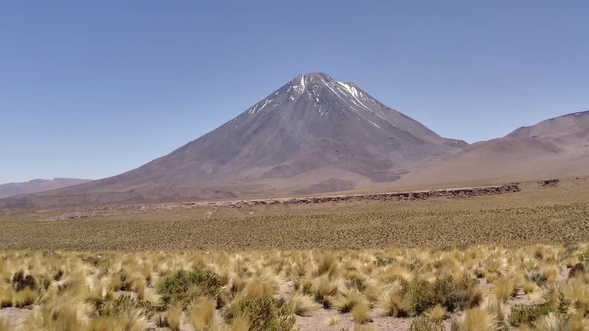 Desert brush leads up to a mountain dusted with snow at the peak