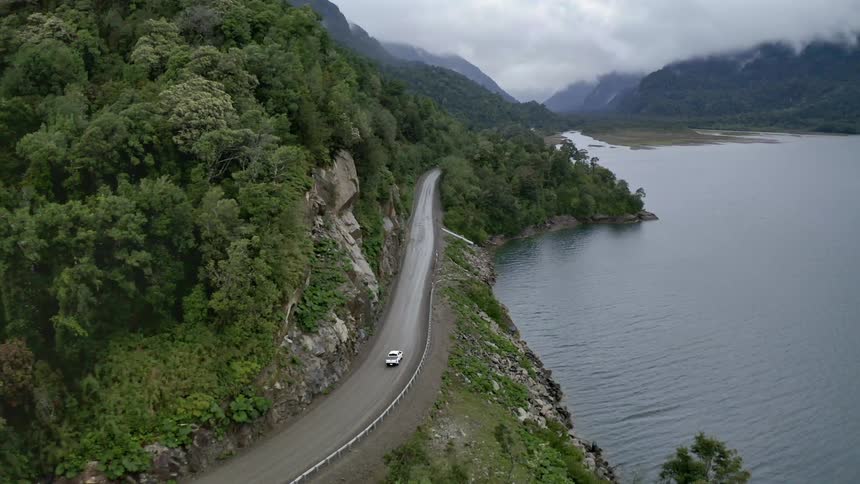 Car drive along road bordered by cliff and sharp drop to a lake