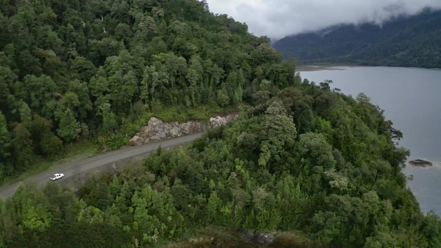 Car drives through forest highway next to the lake on a cloudy day