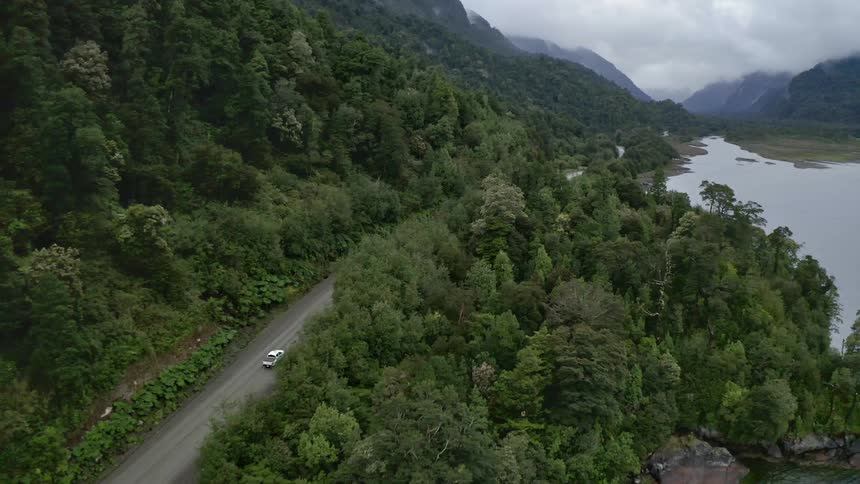 Car drives on road between mountains and lake in forest
