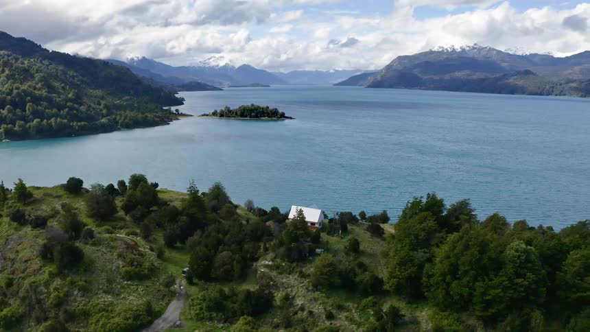 A house at the edge of a lake surrounded by mountains