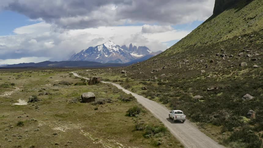 A white truck travels on a dirt road with snowy mountains in the distance