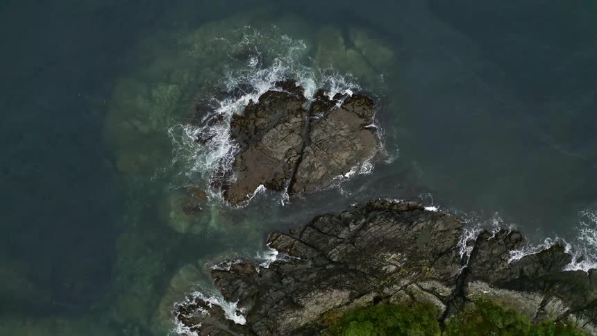 Aerial view of large rock formation in the sea as water crashes around it